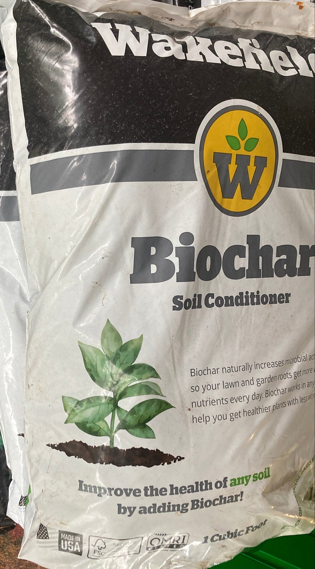 Bag of Wakefield Biochar Soil Conditioner on a surface with a green container in the background.