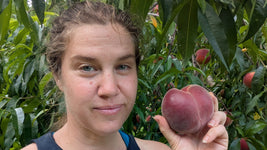 Woman holding a peach in front of a peach tree